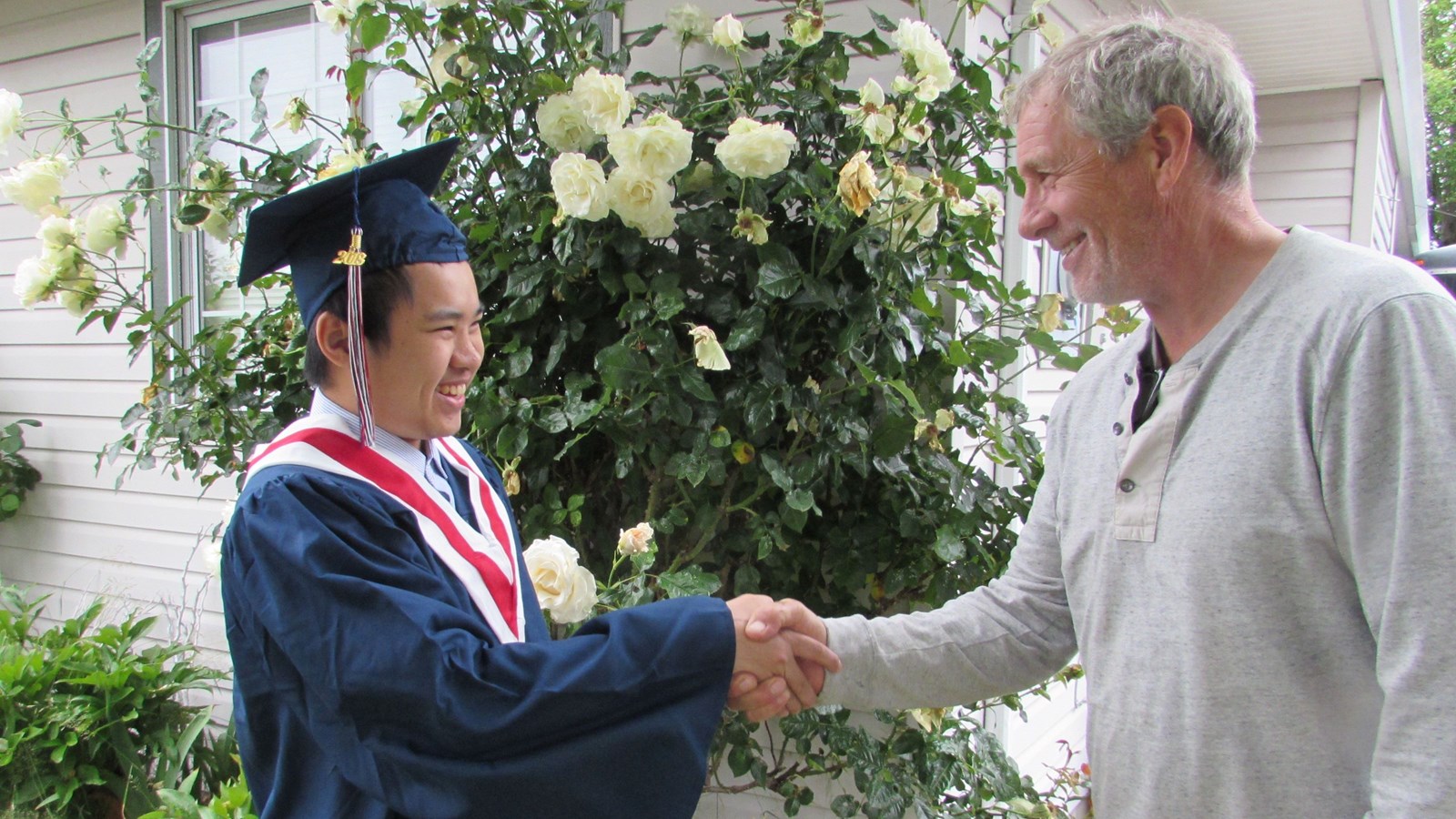 Smiling graduate shaking hands with host family.